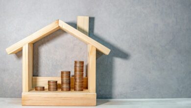 Coins-stacked-in-wooden-house-frame-on-table.-Home-mortgage-loan-rate.-cm