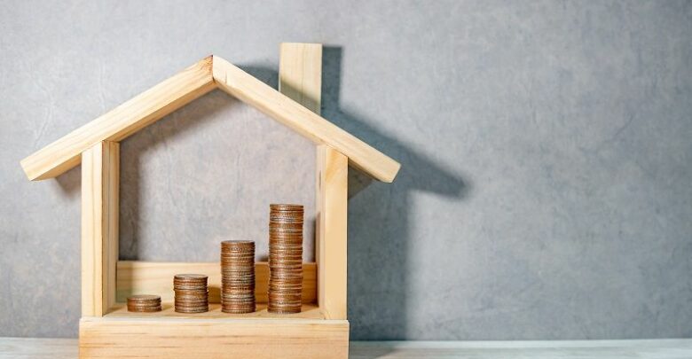 Coins-stacked-in-wooden-house-frame-on-table.-Home-mortgage-loan-rate.-cm