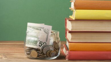 Jar stufffed with $50 bills on desk by schoolbooks
