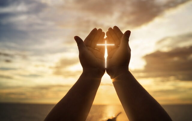 Hands cupped around the sunrise with a cross shining through