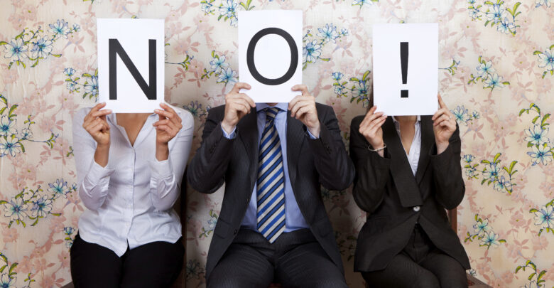 Three people holding the word NO! over their faces